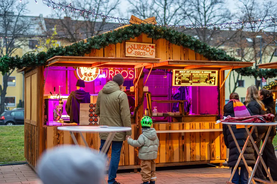 Ein Vater mit Kind vor der leuchtenden Churros-Hütte