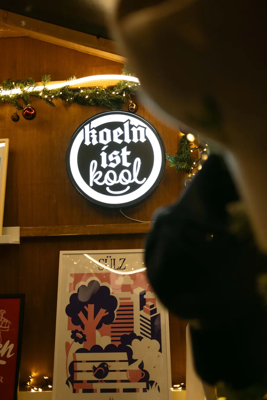 Leuchtschild „koeln ist kool“ und ein Sülz-Poster in einer Shop-Hütte